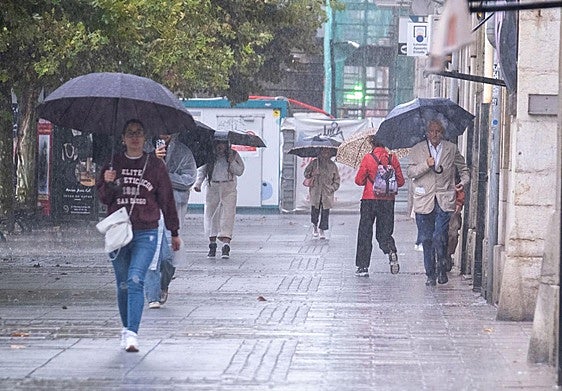 Viandantes se refugian con su paraguas de la intensa lluvia caída este lunes en Santander.