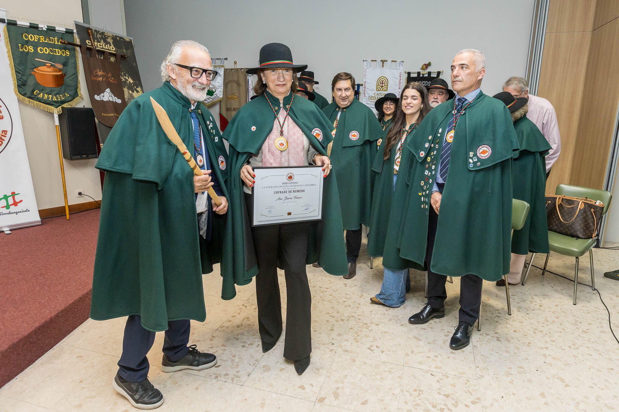 Alfonso Fraile, presidente de la Cofradía de los Cocidos de Cantabria, nombra a Ana Barca nueva cofrade de la familia gastronómica, frente al resto de nuevos integrantes. 