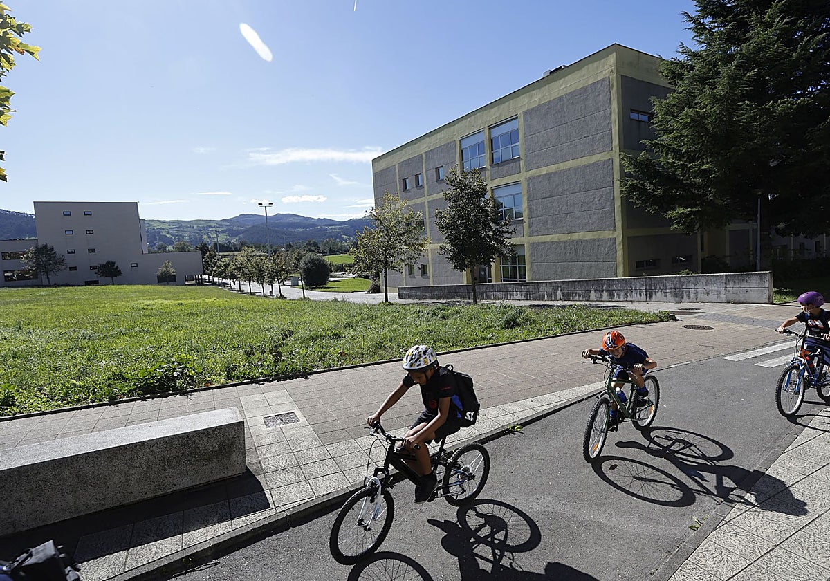 Tres niños circulan con su bicicleta por el campus universitario.