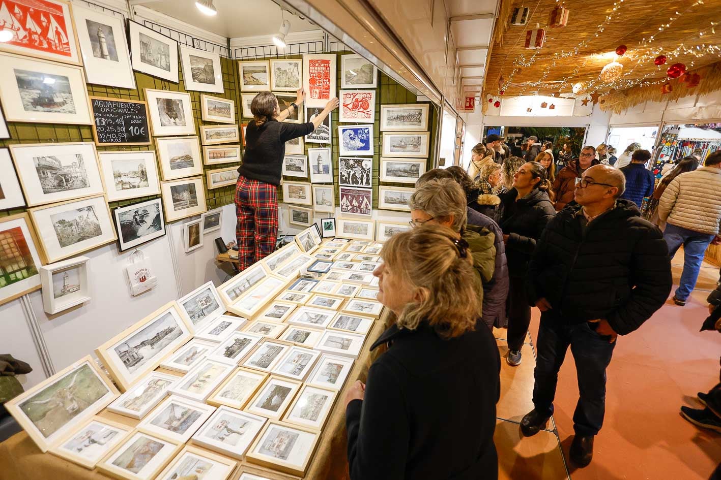 Varias personas observan un puesto de láminas del mercado navideño de Pombo.