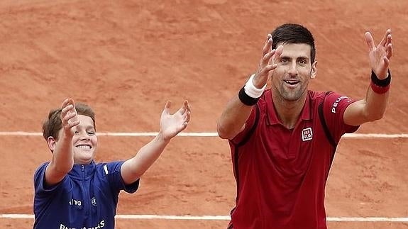 Novak Djokovic bromea con un recogepelotas tras su triunfo ante Bautista. 