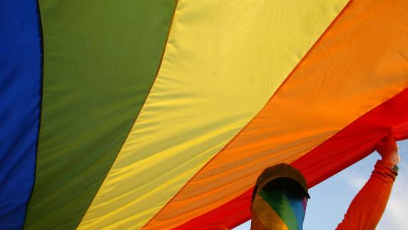 Un hombre sujeta la bandera del orgullo gay.