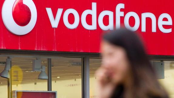 Una mujer camina, hablando por el móvil, junto a un establecimiento de Vodafone.