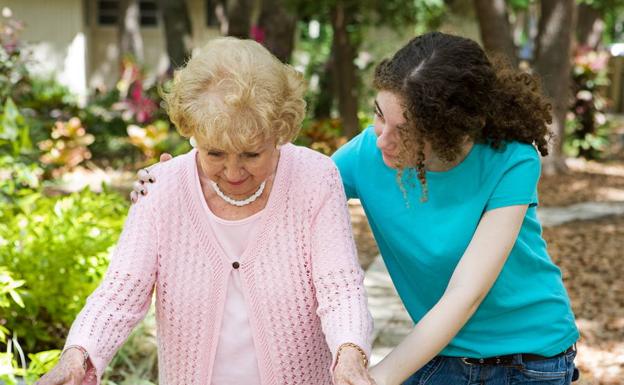 Una mujer ayuda a caminar a una persona mayor.