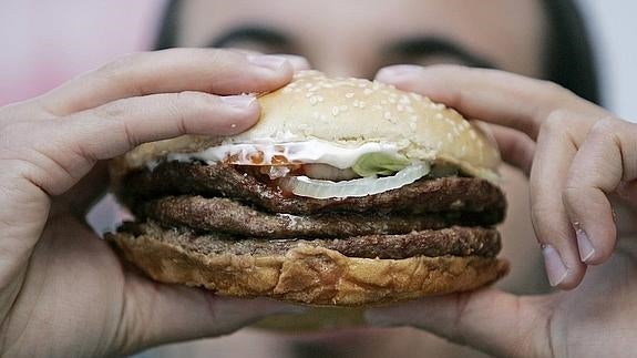 Un joven se dispone a ingerir una hamburguesa.