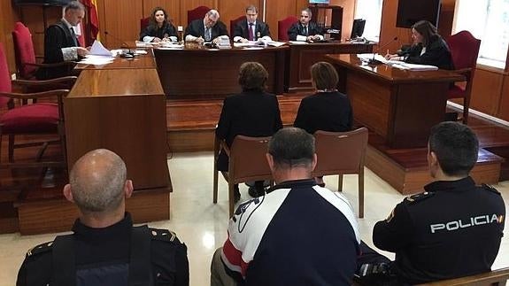 El acusado, de espaldas entre dos policías, esta mañana en la Audiencia.