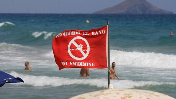 Bandera roja en una playa mientras los bañistas ignoran la prohibición