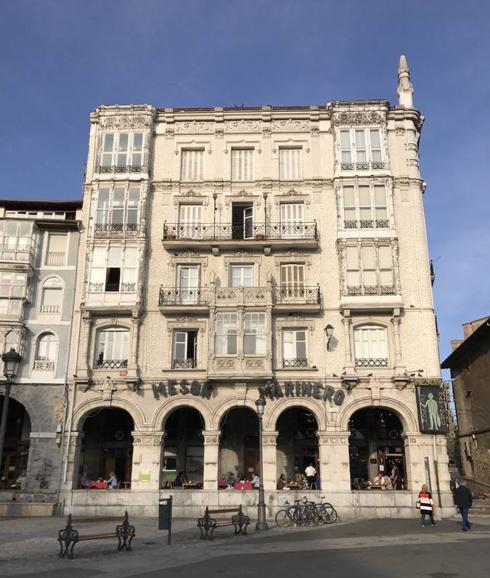 El restaurante se ubica en los bajos de este edificio declarado Bien de Interés Cultural en 1991. Se trata de un edificio de estilo neogótico e influencia modernista, uno de los edificios de viviendas más sobresalientes de Castro Urdiales. Proyectado a principios del siglo XX por Severino de Achúcarro, se ubica en la Plaza del Ayuntamiento junto al puerto.