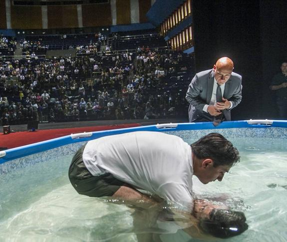 Uno de los testigos recibe el bautismo sumergiéndose en la piscina con el apoyo de un ayudante. 