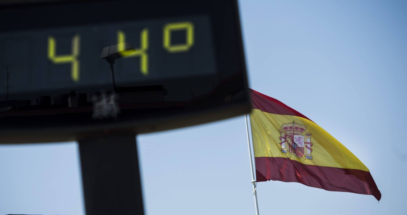 Una bandera española ondea junto a un termómetro callejero de Córdoba que marca 44 grados.