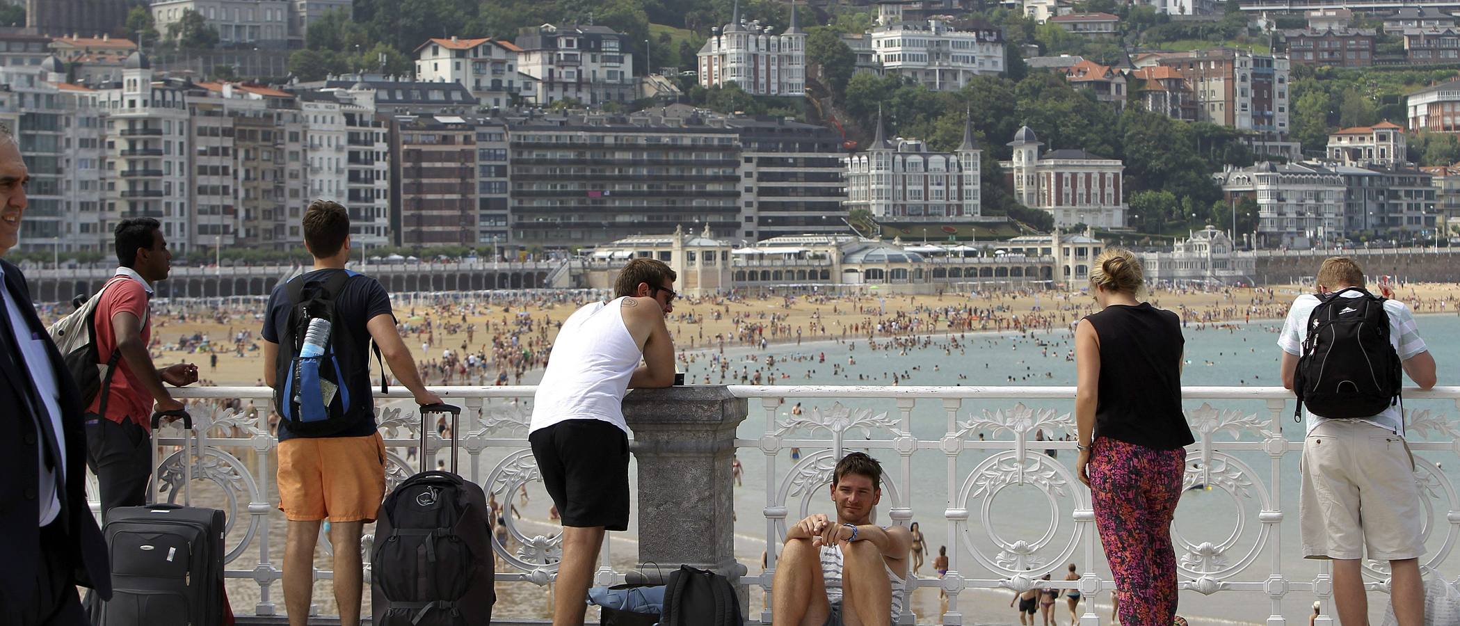 Varios turistas descansan junto a la barandilla de playa de La Concha de San Sebastián donde hoy se siguen registrando altas temperaturas.