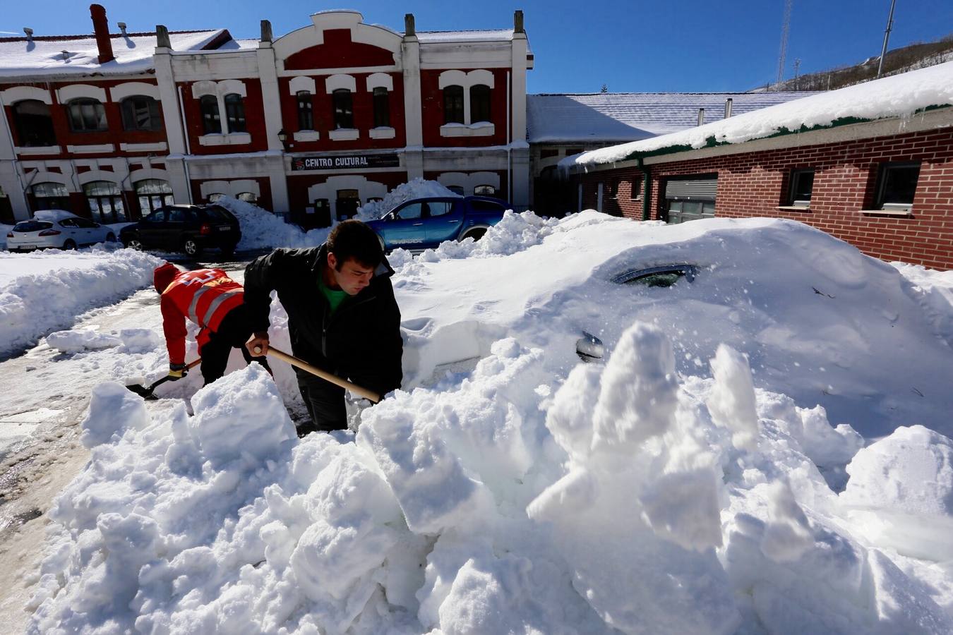 Unos voluntarios de Cruz Roja ayudan a una mujer a quitar la nieve de su vehículo en Barruelo de Santullán.