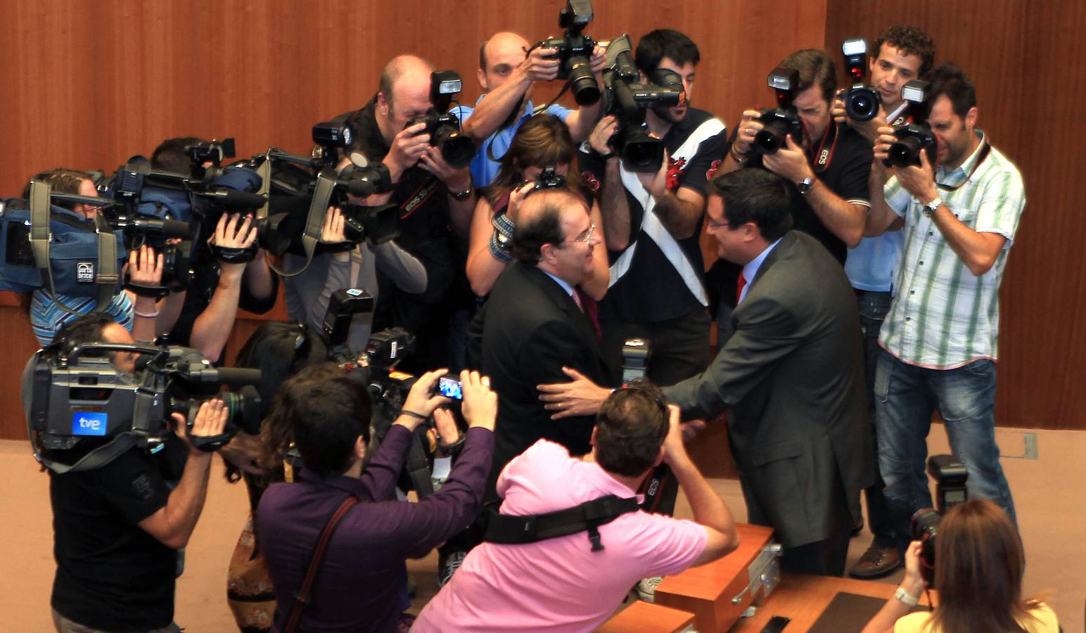 Los medios siguen a Juan Vicente Herrera que cruza el hemiciclo de las Cortes hacia la bancada socialista para saludar a Óscar López. Finalmente, los líderes se aprietan la mano momentos antes del debate de investidura