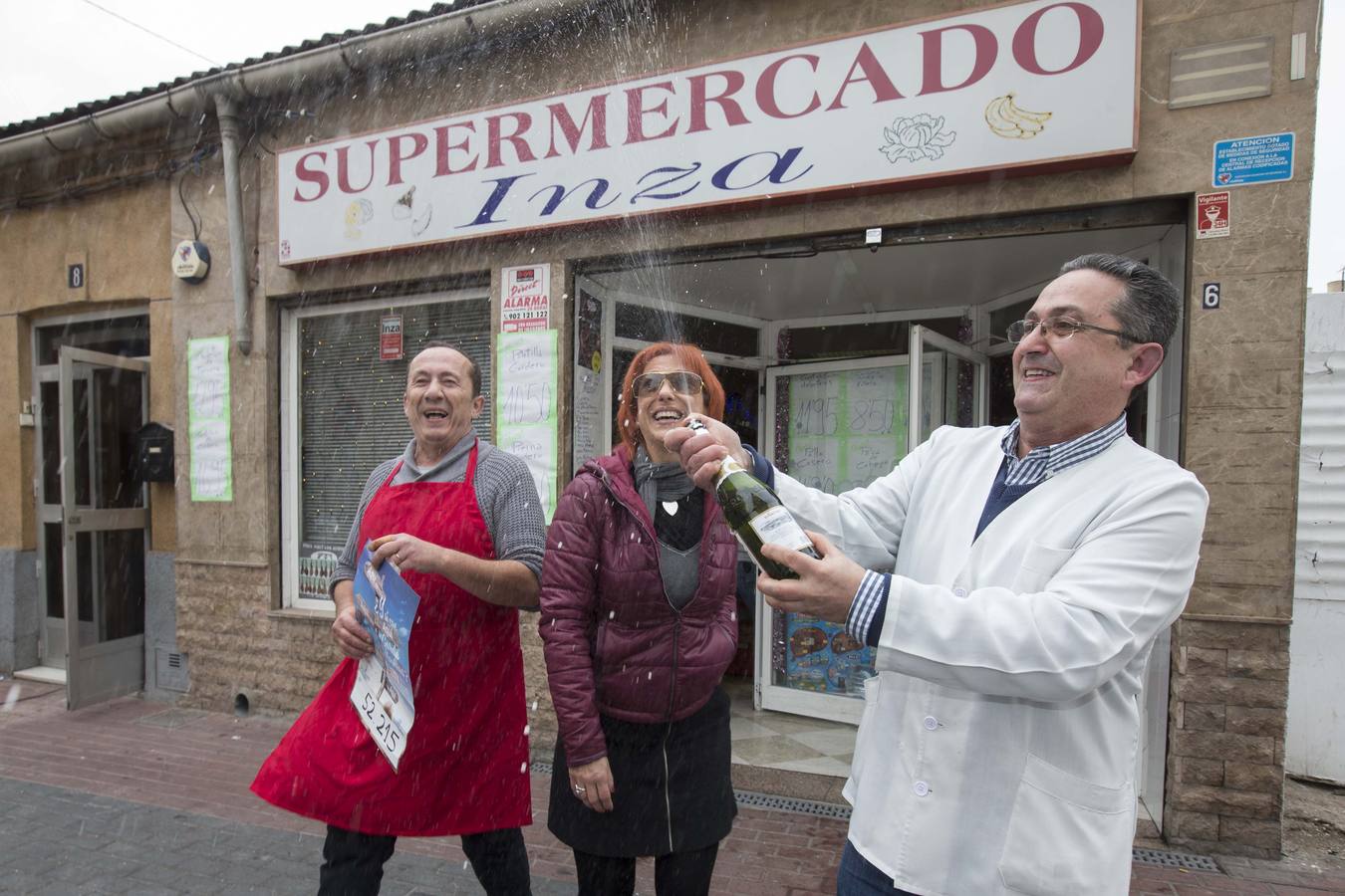 El propietario del supermercado Inza, José Nicolás Inza (d), junto a su mujer Camen Valls, y el carnicero Antonio Hernández (i), celebran un cuarto premio, el 52215.