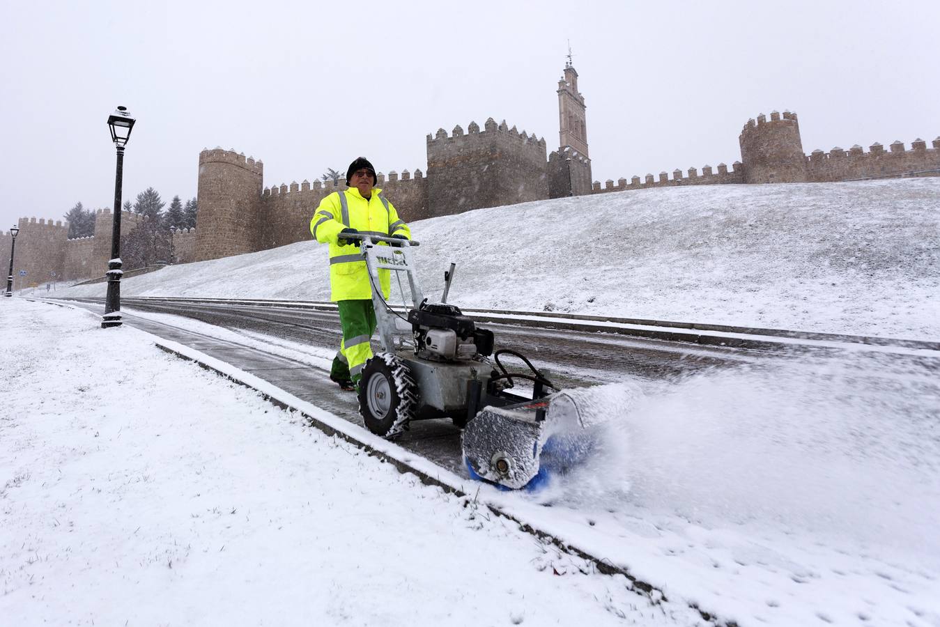 Un operario retira la nieve caída durante la noche en una calle de Ávila junto a la muralla.