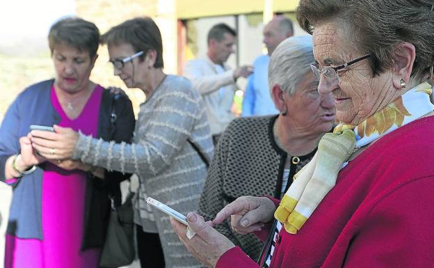 Vecinas de Magaña consultan sus teléfonos móviles.