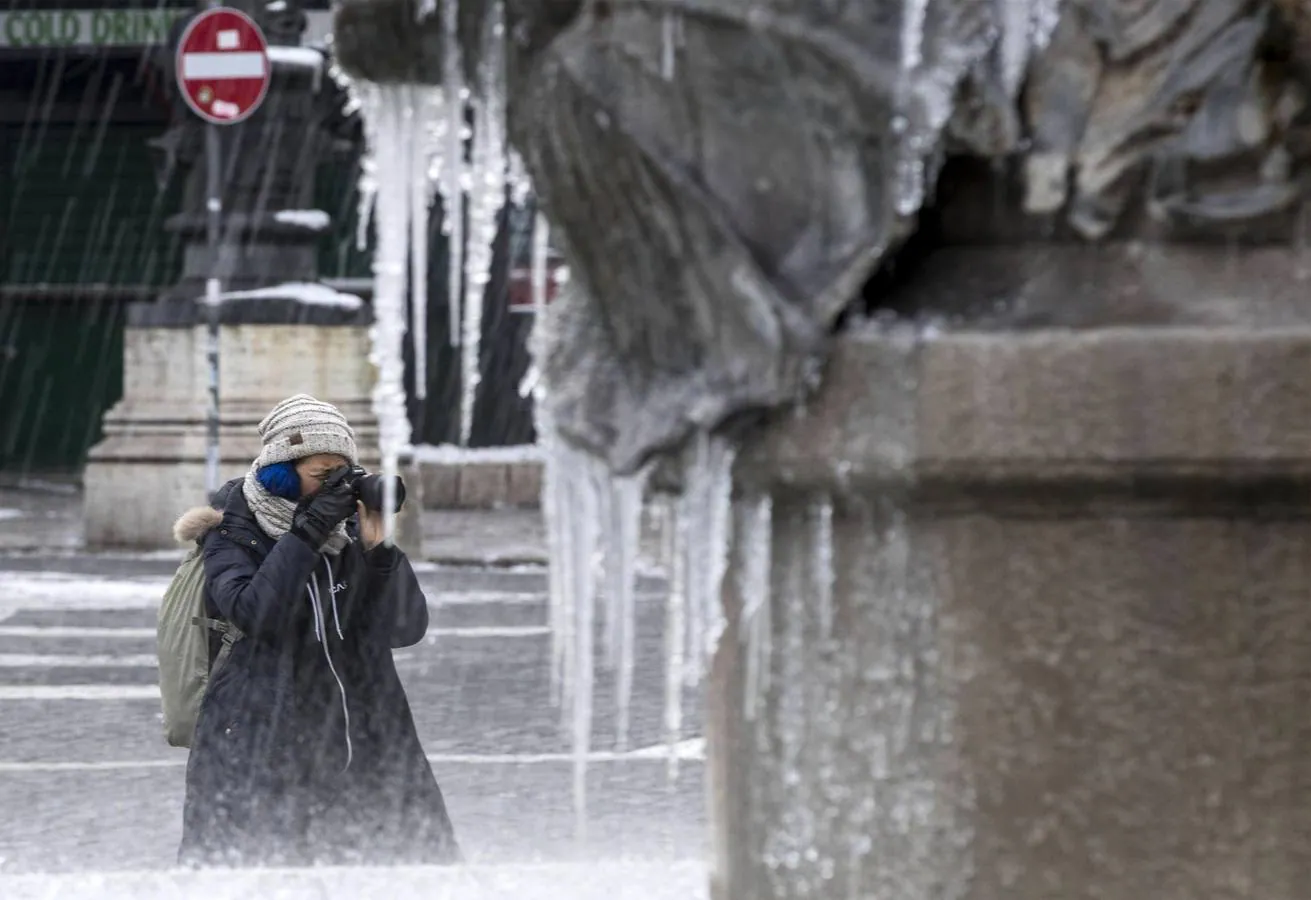 Un turista toma fotos de una fuente cubierta carámbanos de hielo en el centro de Roma.