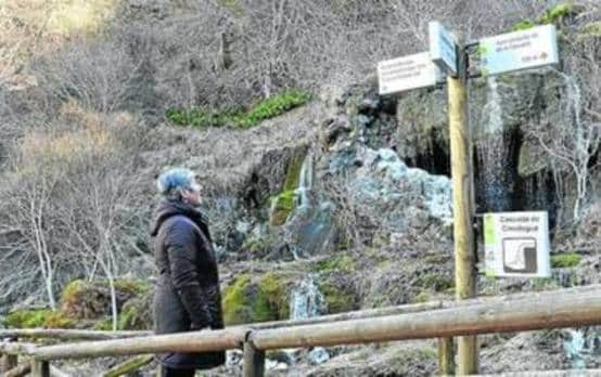 Una mujer lee el cartel informativo de la cascada de Covalagua. 