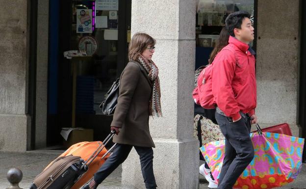 Varios turistas con maletas y bolsos caminan por una calle de Segovia. 