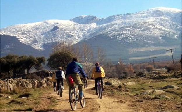 Un grupo de ciclistas circula por Guadarrama, con la sierra al fonso. 