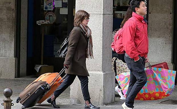 Unos turistas transitan por una cnétrica calle de Segovia con sus maletas y equipajes. 