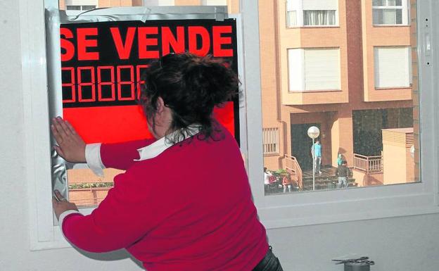 Una mujer coloca el cartel de 'se vende' en un piso de la capital segoviana. 