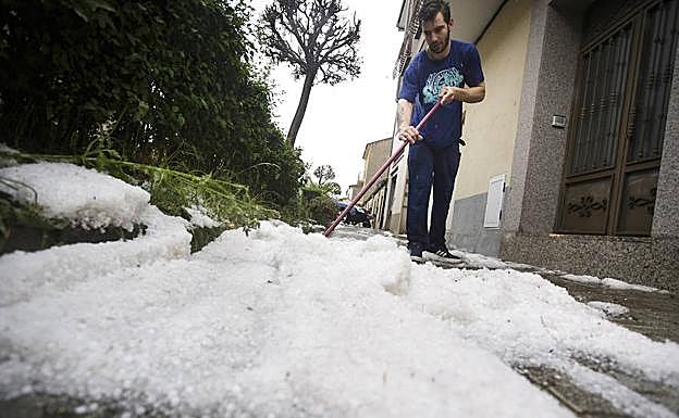 Un joven retirando el granizo a la puerta de una vivienda. 
