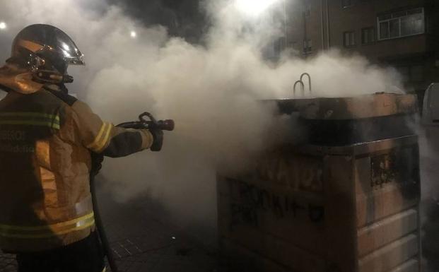 Un bombero sofoca uno de los contenedores quemados.