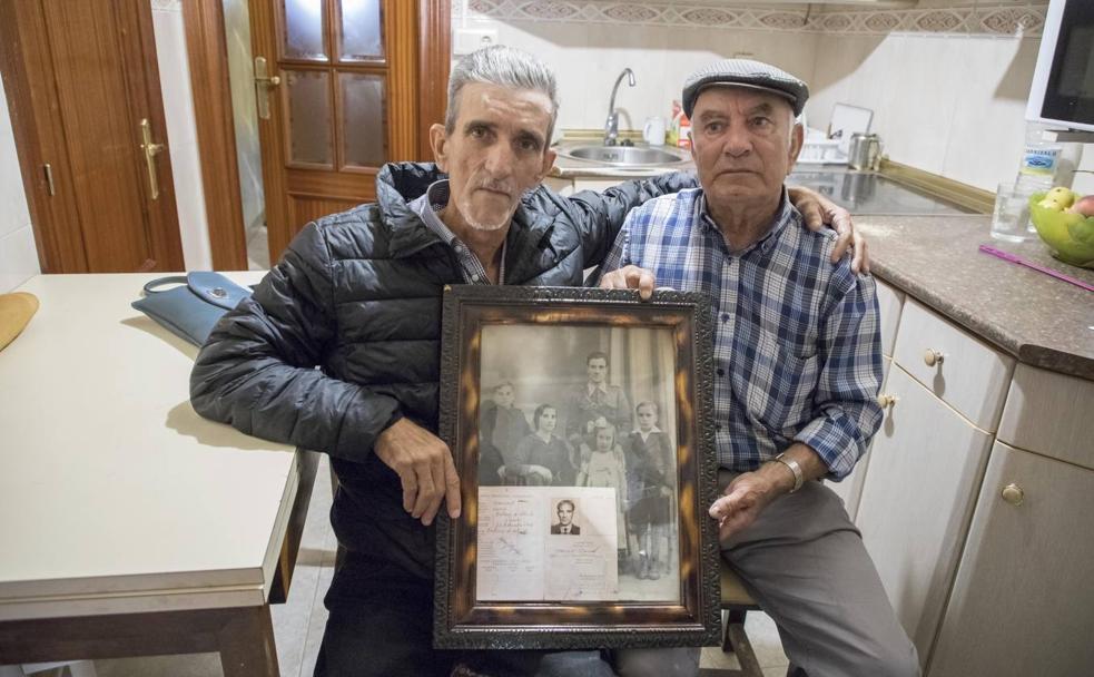 Los dos hermanos posan en la casa del pueblo donde nació su padre con una fotografía y el pasaporte de su padre.