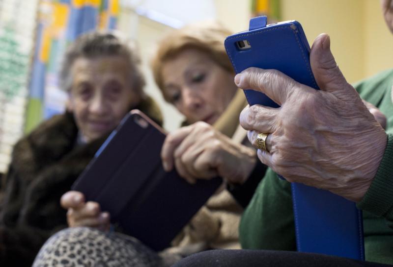 Una mujer sostiene un móvil. Al fondo, Marisa y Herminia miran la pantalla. Son de la Asociación de Nuestra Señora de Tiedra Vieja, en Tiedra, y participan en las aulas de cultura de la Diputación. 