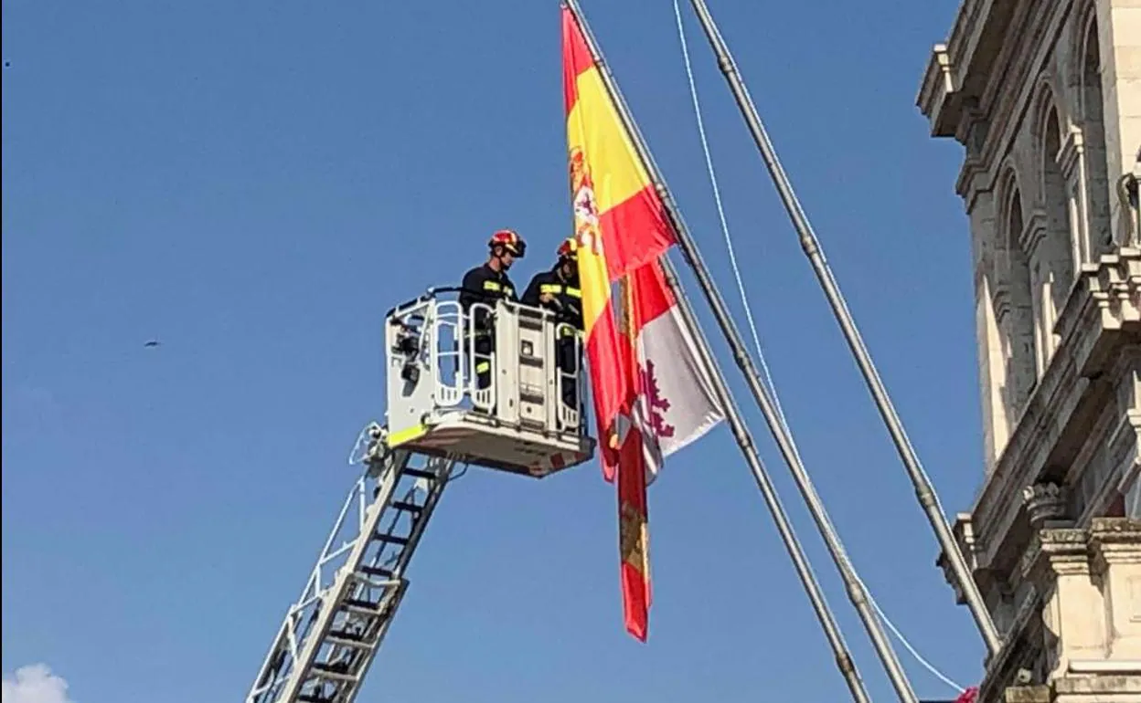 Dos bomberos, en la escala, junto a las banderas.