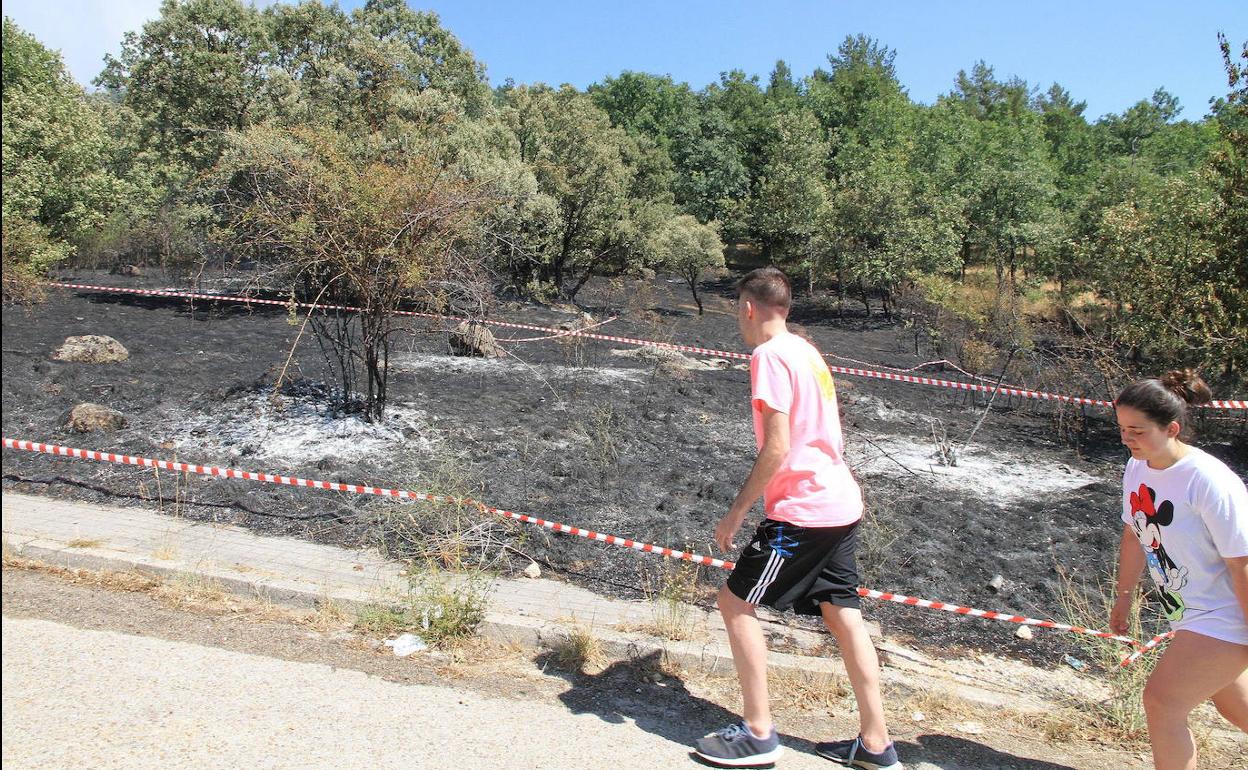Dos jóvenes suben por un camino junto a un tereno arrasado por las llamas en La Granja. 