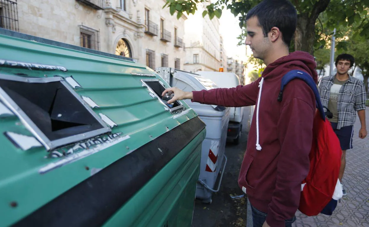 Un joven deposita residuos en un contenedor verde.