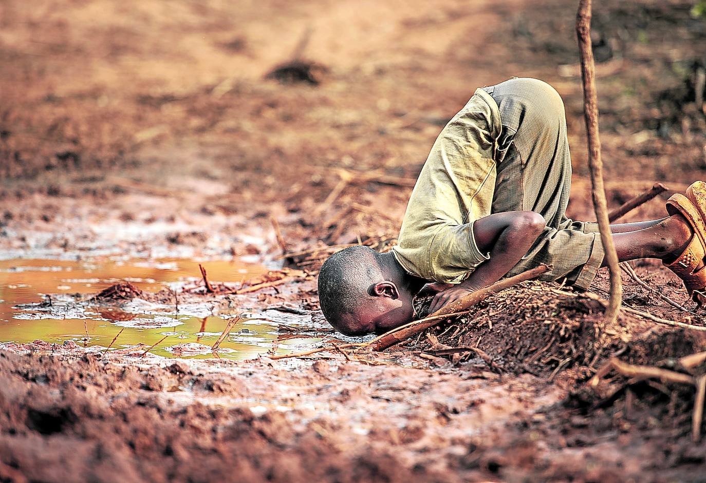 Un niño bebe agua de un charco en Kakamega, Kenia.