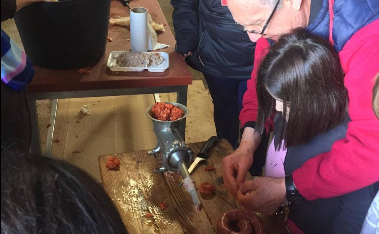 Un adulto muestra a una niña cómo realizar el embutido de chorizo. 