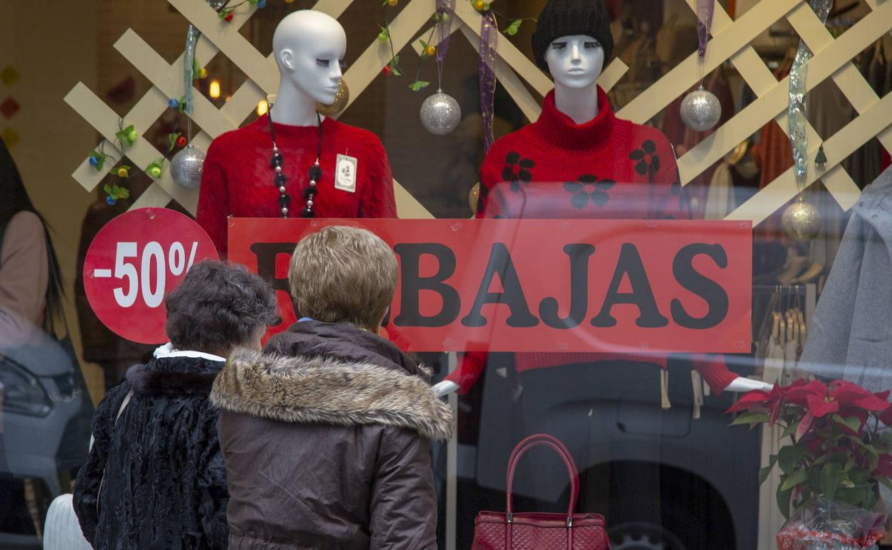 Dos mujeres observan el escaparate de un comercio que anuncia rebajas en sus productos. 