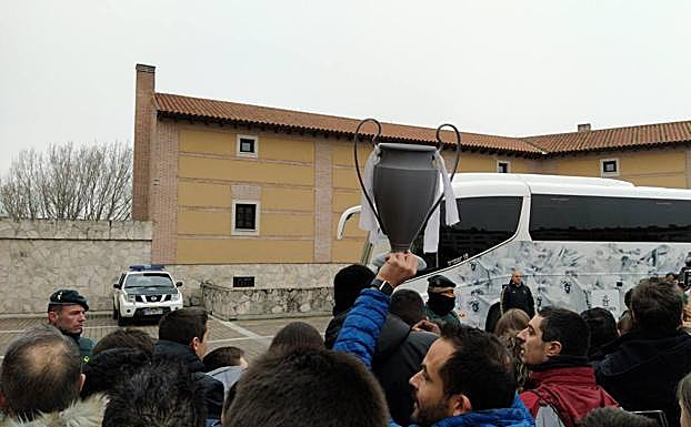 Un aficionado levanta una Copa de Europa hecha de cartón a la llegada del Real Madrid. 