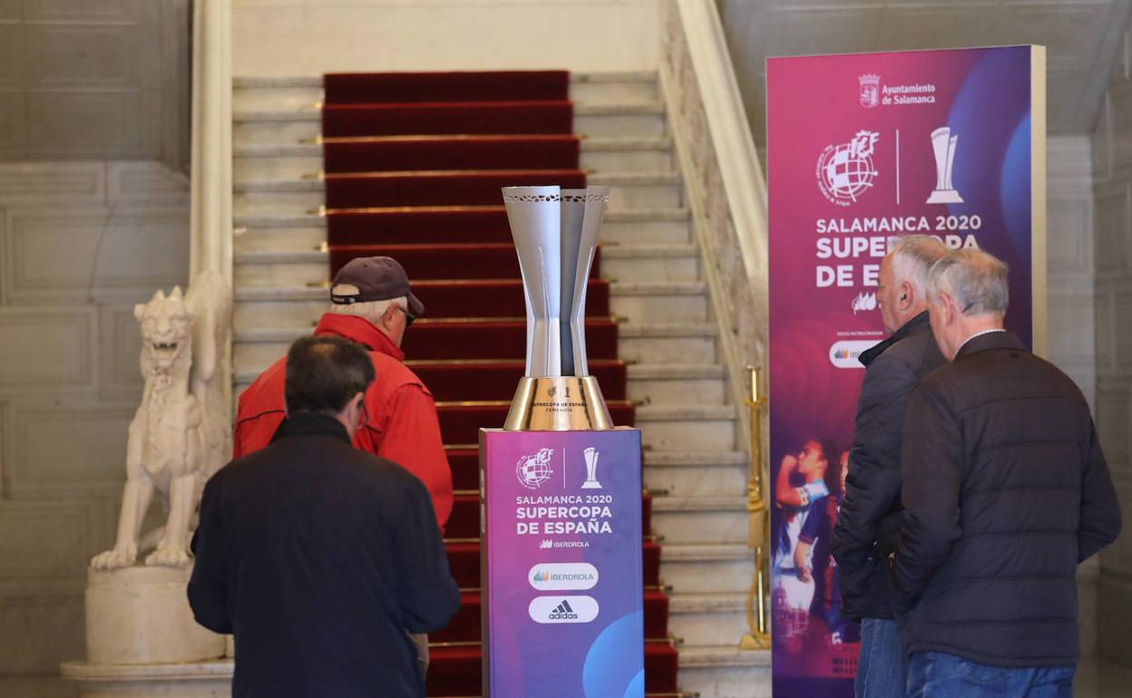 Varias personas observan el trofeo en el zaguán del Ayuntamiento.