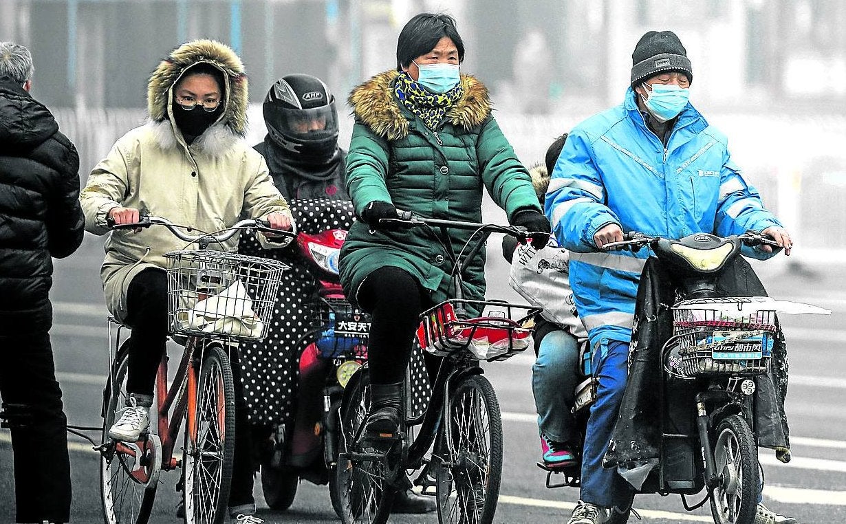 Ciclistas protegidos por mascarillas circulan por las calles de Pekín, mucho más tranquilas que de costumbre.