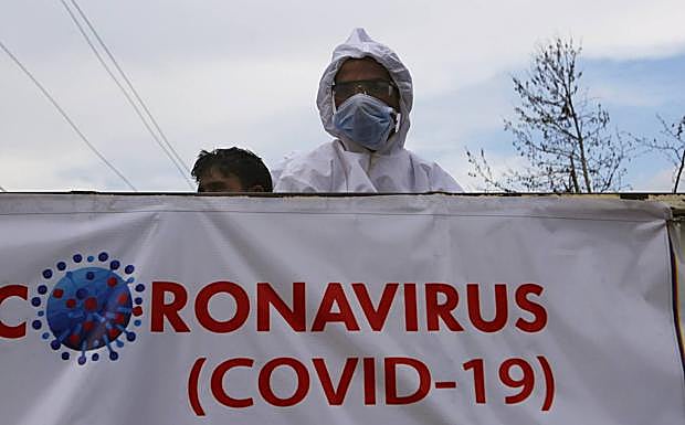 Un hombre se protege con máscara y traje aislante en un pueblo de India tras un cartel sobre el coronavirus.