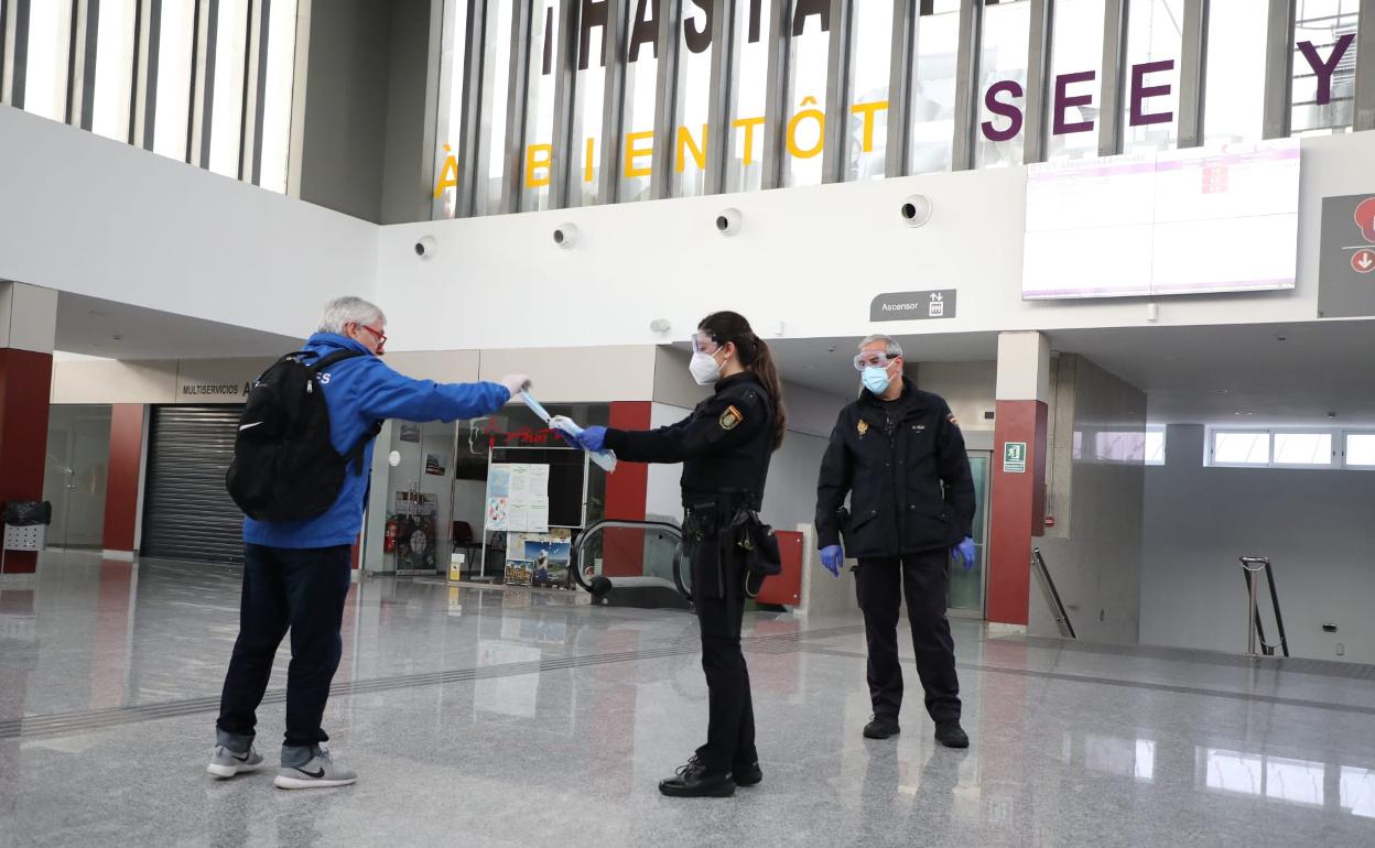 Una policía nacional entrega una mascarilla a una persona en la estación de autobuses de Salamanca.