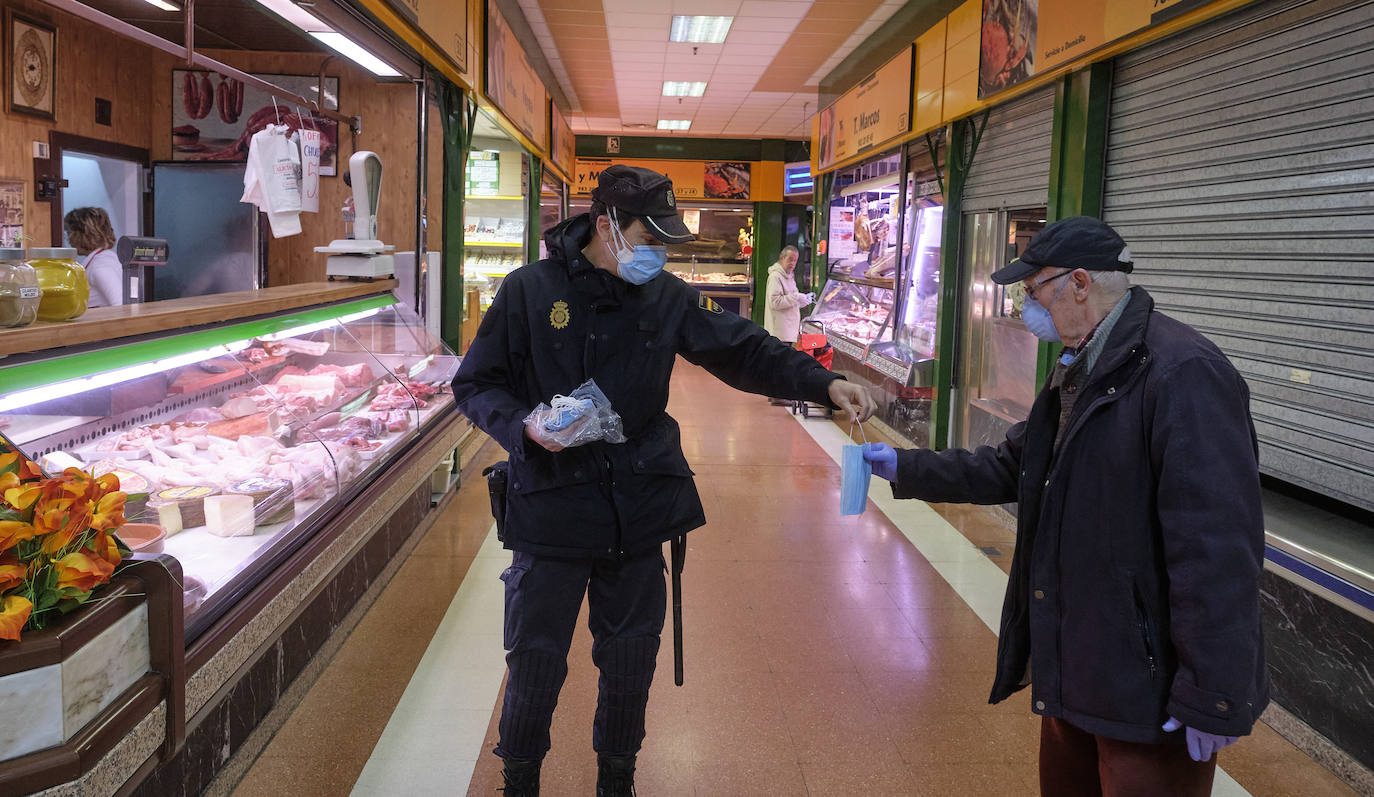 Un policía nacional distribuye mascarillas a clientes e industriales del mercado del Campillo.