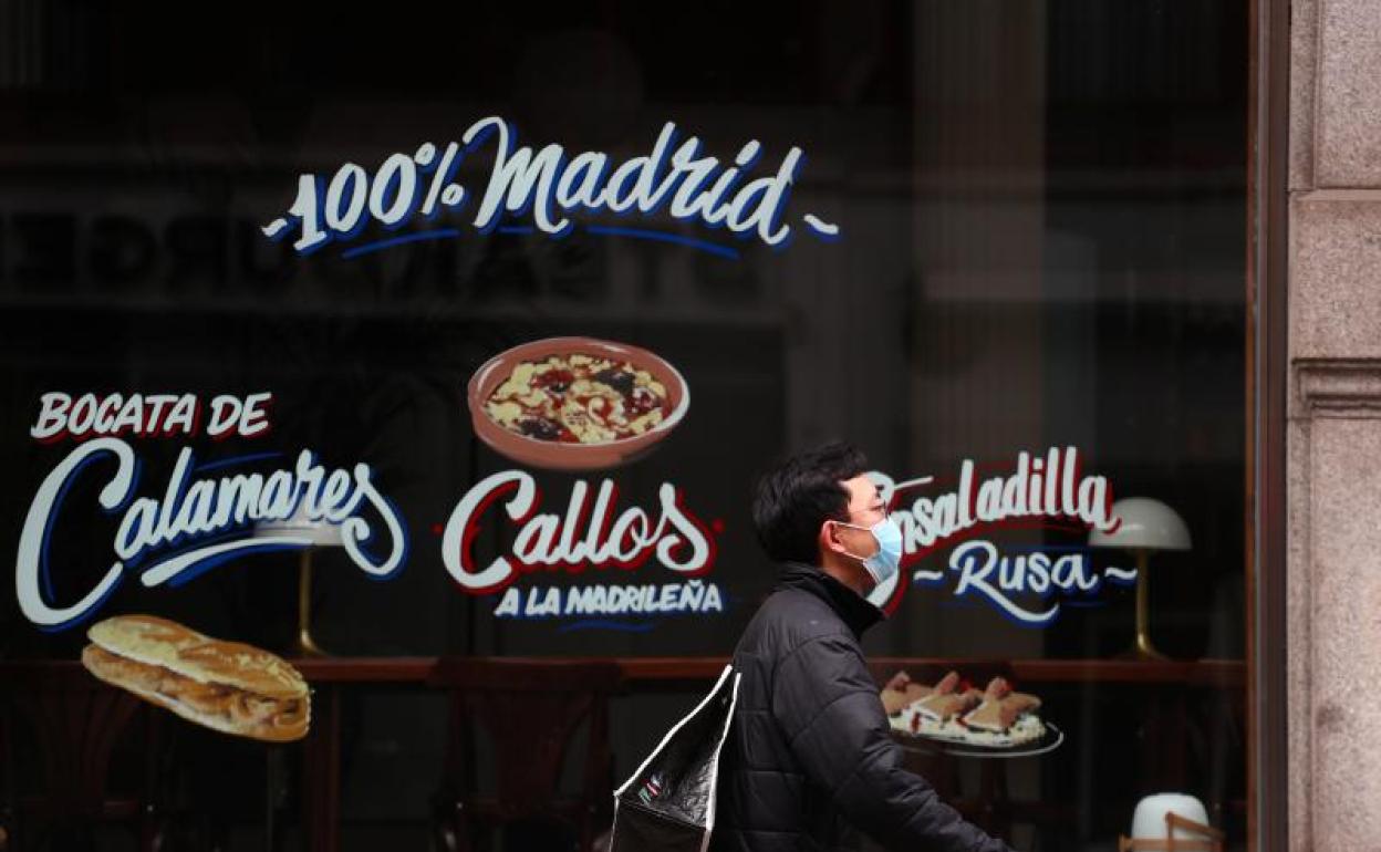 Un hombre con mascarilla pasa frente a un restaurante cerrado en Madrid. 