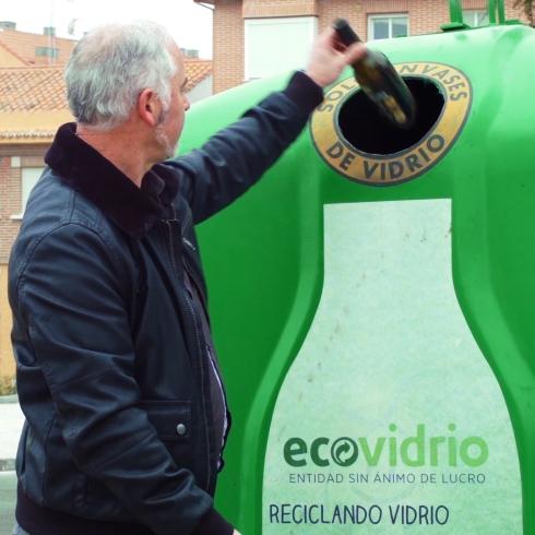 Un ciudadano introduce una botella de vidrio en un contenedor verde. 