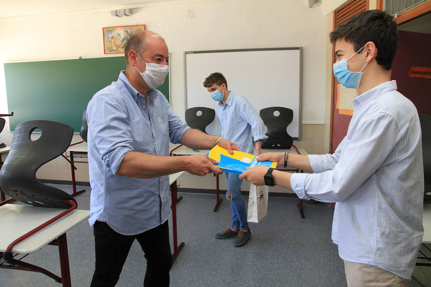 El profesor Sergio Calleja entrega unos libros a uno de sus alumnos de los Maristas.