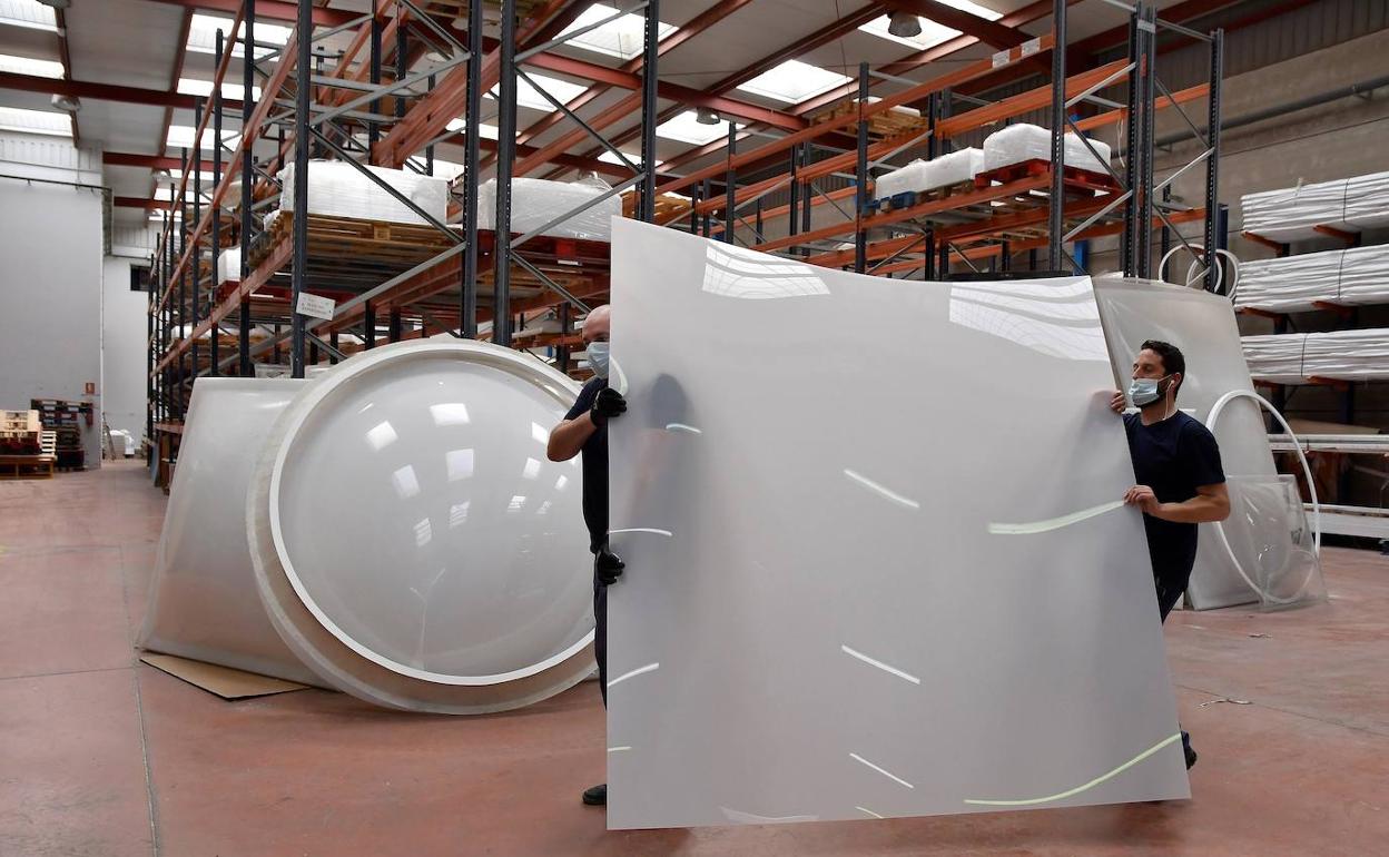 Unos trabajadores transportan una plancha de metacrilato en una empresa de plásticos.