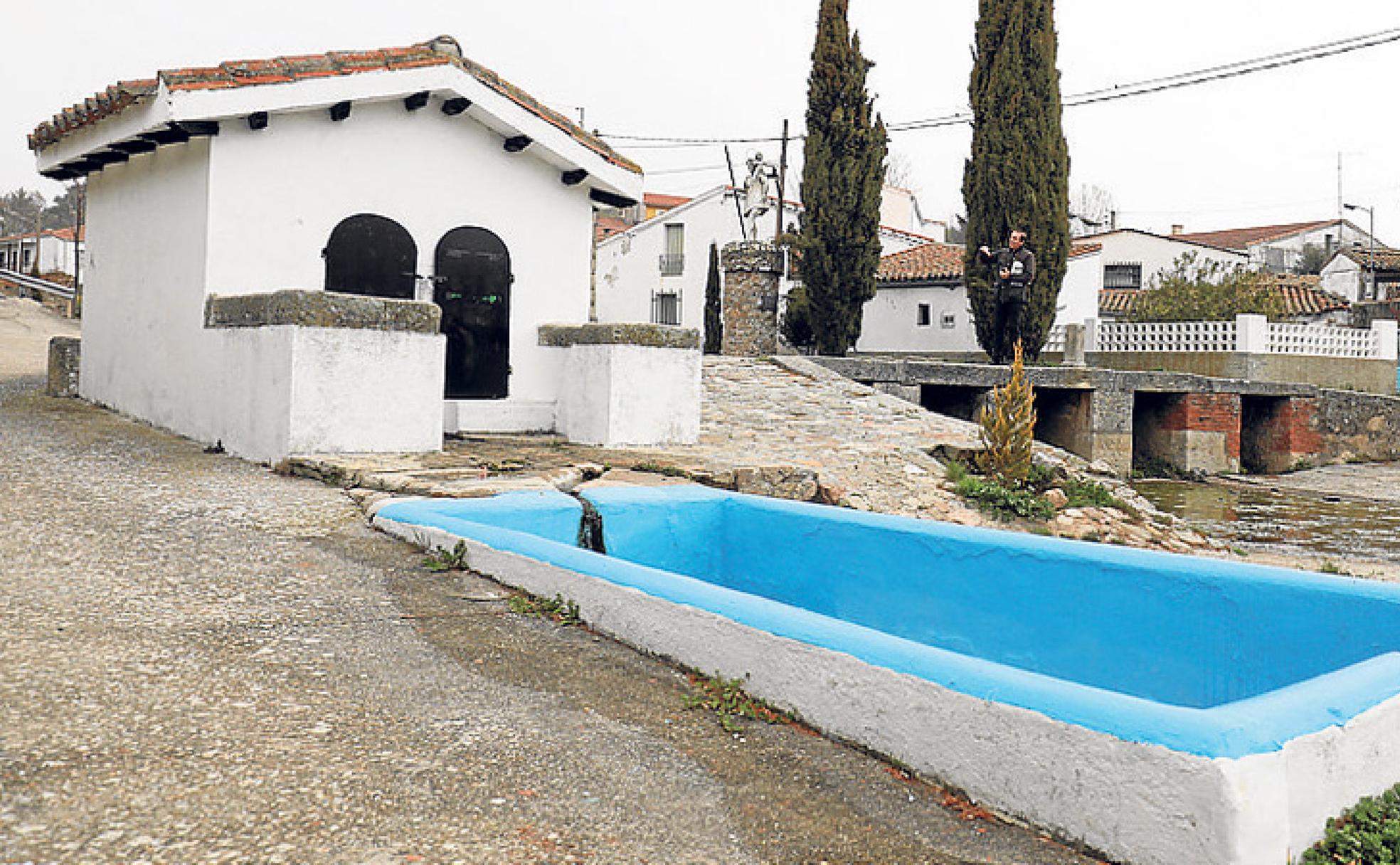 Fuente natural, cerrada por unas puertas, de la que sale el agua a un pequeño estanque y a la derecha, la ermita.