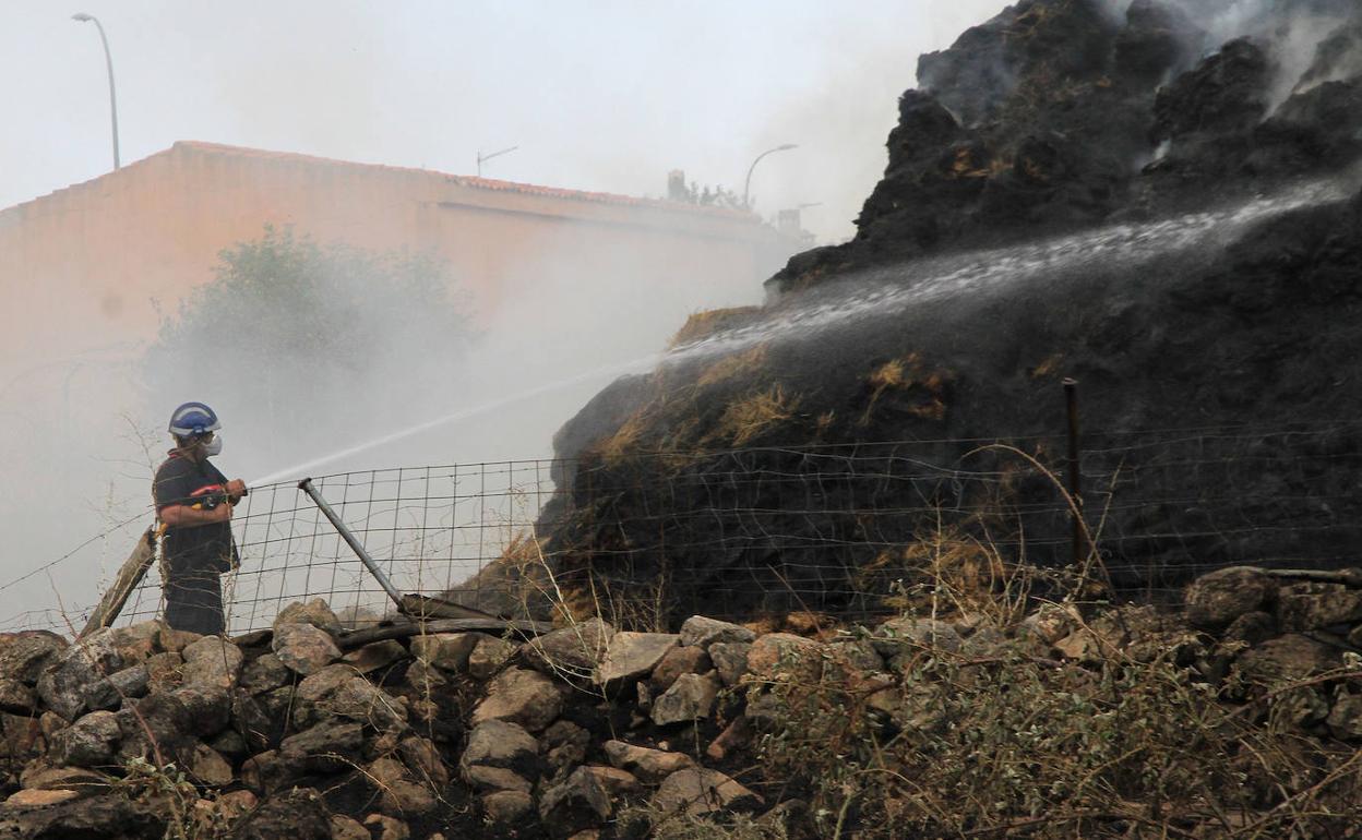 Un bombero lanza agua contra el montón de pacas de paja que esta mañana continuaba ardiendo, aunque controlado. 
