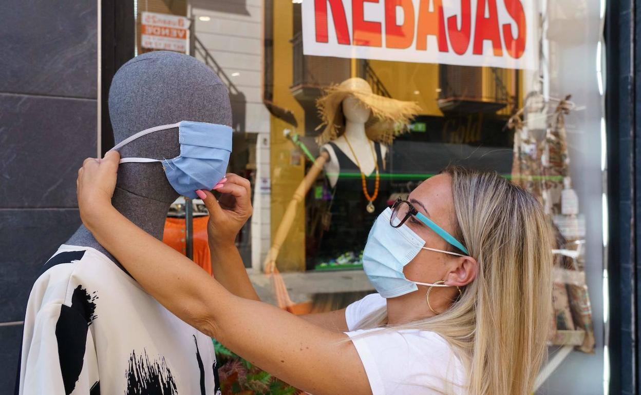 Una mujer coloca una mascarilla en un maniquí a la puerta de un comercio. 