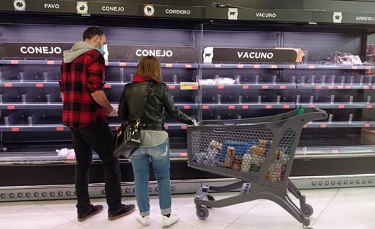 Dos jóvenes, ayer ante una de las estanterías de un supermercado vacío de existencias.